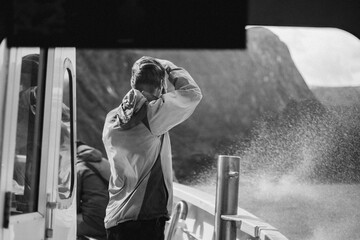 Tourist man takes picture on windy boat tour in Milford Sound