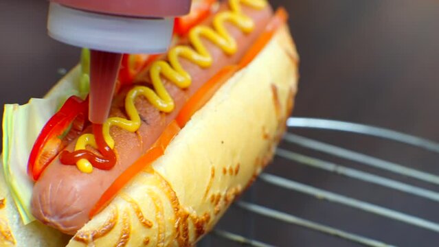 Tasty hot dog with grilled sausage . Adding ketchup to hot dog	