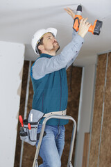 male builder drills a hole in the ceiling