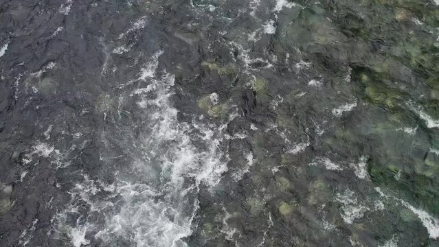 Slow, tight, tilting shot of fast flowing, choppy river water, approaching a large waterfall in Norway.