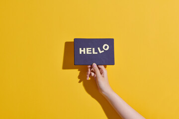 Hand holding hello card on yellow background