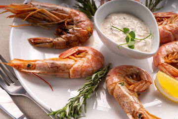 Fried shrimp with creamy sauce served on a white plate with lemon and rosemary.
