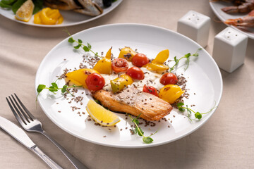 Baked salmon served with tomatoes grill, lemon and microgreen on white plate
