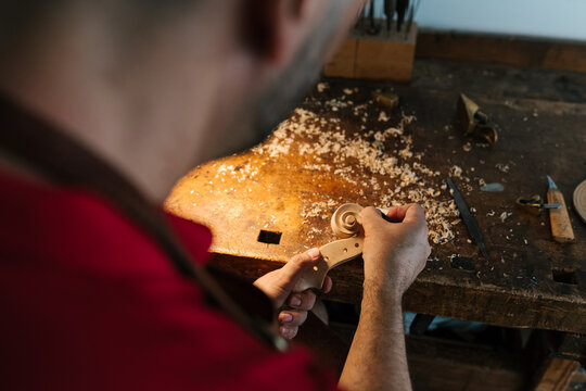 Crop craftsman cutting violin scroll in workplace