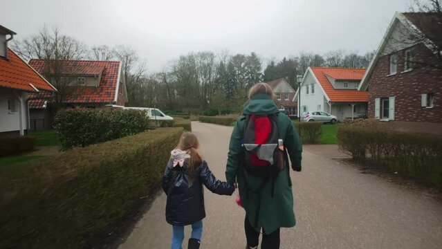 Mother and child with backpack and raincoat walking through bungalow village