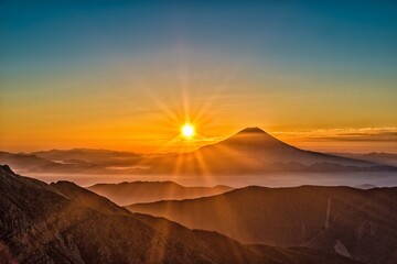 The image showcases the majestic Mount Fuji with the sun rising above its peak, casting a golden glow that illuminates the surrounding landscape in a breathtaking display of natural beauty.