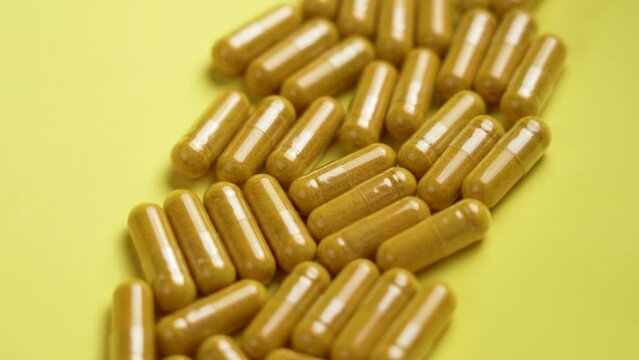 Yellow turmeric tablets with curcumin extract on a coloured background. Alternative medicine concept