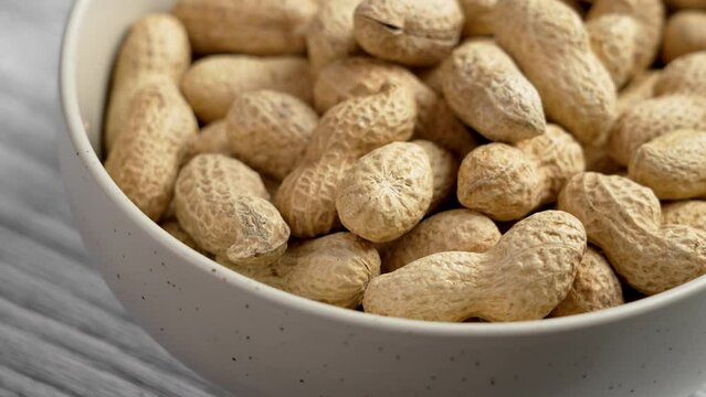 Full ceramic bowl of roasted peanuts in shell. Whole unshelled groundnuts close up. Rotation