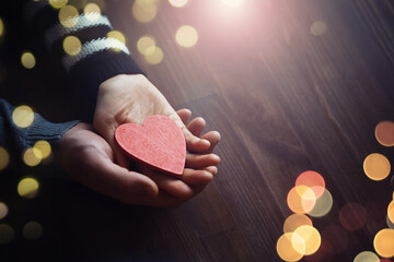 Woman holding hands with red heart on wooden background, top view
