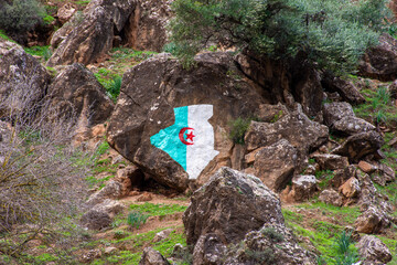Low-angle view of the Algeria flag painted on a rock formation in the mountain.