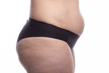 Fragment of a feminine figure with excess weight in black panties. Stretch marks and belly fat. Isolated on a white background. Close-up. Side view. Health and beauty.
