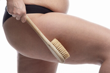 A woman massages her thighs with cellulite with a brush. Excess weight, health and cosmetology. Close-up. Isolated on a white background.