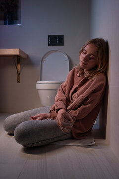 Drunk woman sitting on floor near toilet
