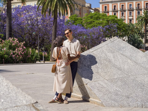 Diverse couple hugging in city against blooming trees