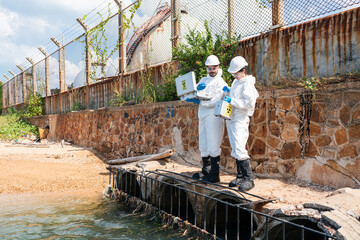 Scientists biologists and researchers in protective suits taking water samples from waste water...