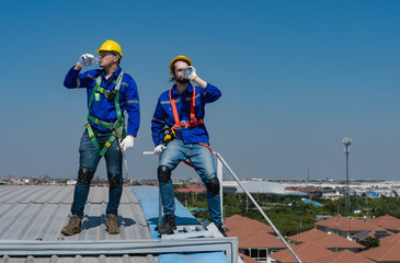 Roofer men drinking water at breaktime after working hard on building roof