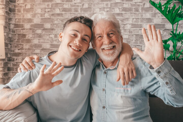 Portrait of happy family couple, young boy and his old grandfather hugging looking at camera waving...