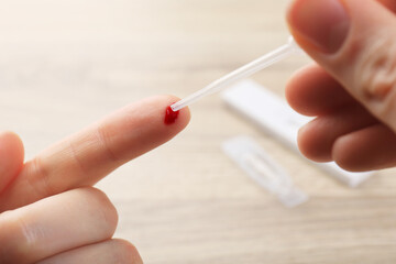 Laboratory testing. Woman taking blood sample from finger with pipette on blurred background,...