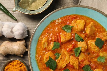 Delicious chicken curry and ingredients on wooden table, flat lay