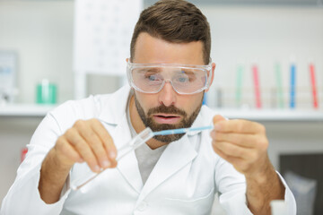 young scientist pipetting blue liquid into test tubes close up