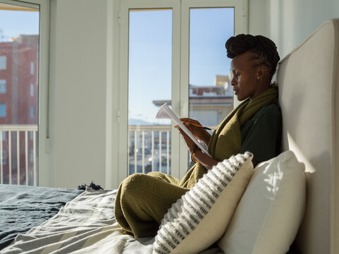 Black lady reading notes in bedroom on sunny day