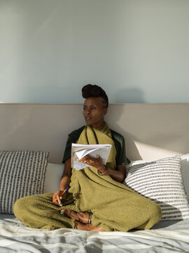 Thoughtful black woman sitting on bed with notebook