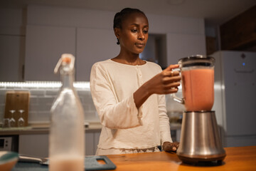 Black woman blending smoothie in kitchen
