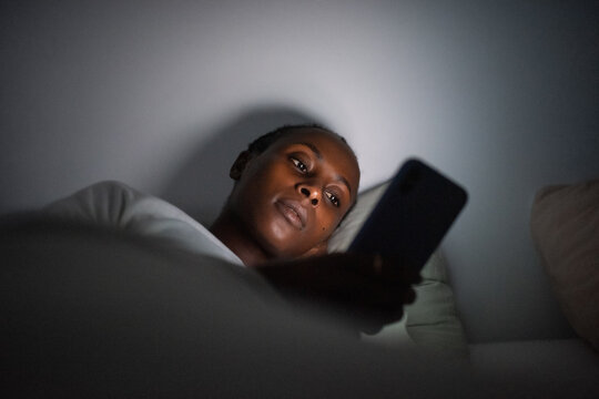 Black woman reading messages via cellphone at night