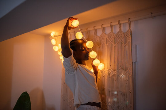 Excited black woman hanging fairy lights at home
