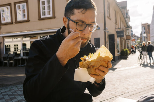 millennial man eating kebab at german restaurant in city