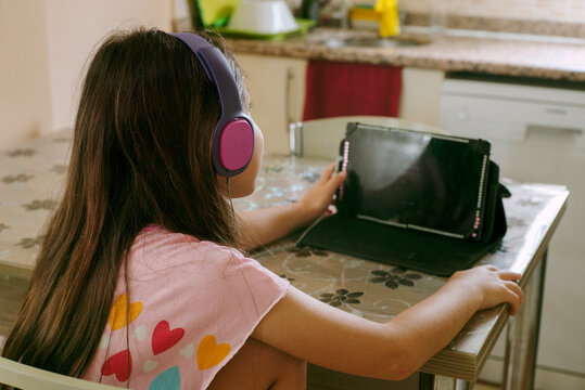 A girl watches a tablet sitting at the kitchen table. 