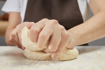 Unknown woman wearing brown apron kneading dough on table sprinkled with flour preparing for baking bread