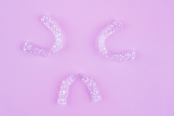 Invisible dental teeth brackets tooth aligners on pink background. Plastic braces dentistry retainers to straighten teeth.