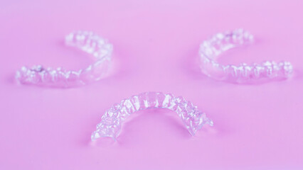 Invisible dental teeth brackets tooth aligners on pink background. Plastic braces dentistry retainers to straighten teeth.