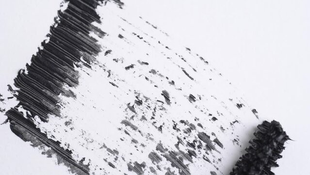 Mascara smudge. Black mascara brush stroke with applicator brush on white background, fashion beauty concept. Close up.