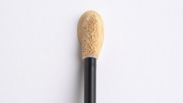 Liquid foundation or bb cream beige color smudge, vertikal swatch. A smear of foundation cream or concealer with a brush on a white background, macro. Texture of cosmetic liquid foundation