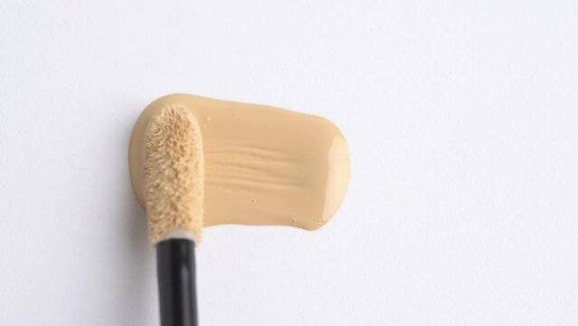 A smear of foundation cream or concealer with a brush on a white background, macro. Liquid foundation or bb cream beige color smudge. Texture of cosmetic liquid foundation