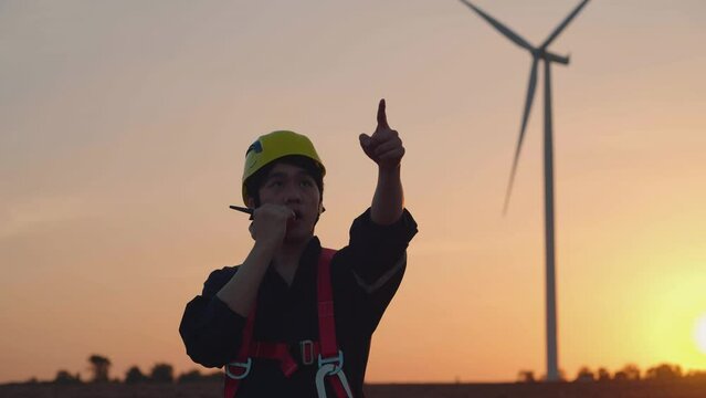 Maintenance engineer using a walkie-talkie for long-distance communication at a wind energy farm, coordinating efficiently with the team amidst turbines. Wind Turbine Engineering, Energy Engineering