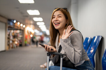 A cheerful Asian female passenger waiting her friends at a waiting seat in the airport terminal.