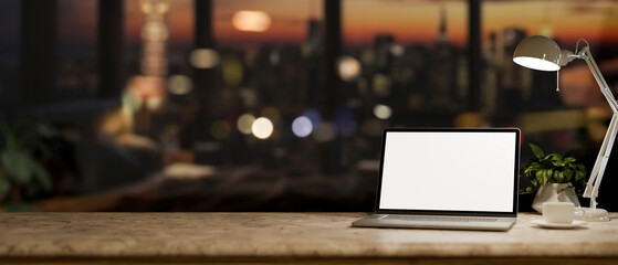 An office desk with a white-screen laptop computer in a modern dark office at night.