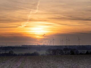 A wind turbine stands tall amid the sunset sky and endless expanse, gracefully harnessing the...