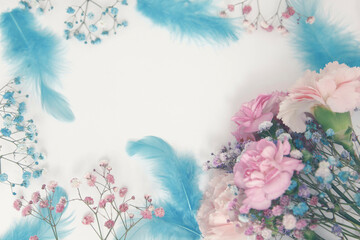 Pastel arrangement in the shape of a frame with space for text. Frame made of flowers and blue feathers.