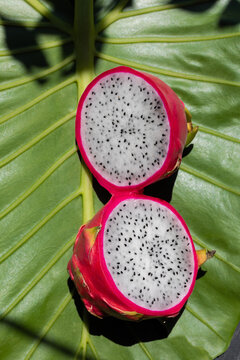 A pink pitahaya split in half on a green leaf 