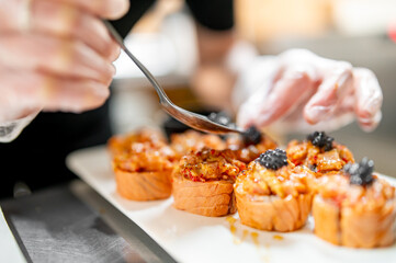The image depicts a chef meticulously garnishing gourmet sushi with a spoon in a professional kitchen setting. The sushi, golden-brown and well-cooked, are arranged on a white plate.