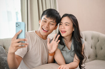 Lovely Asian couple taking selfies with a smartphone together while relaxing in the living room.