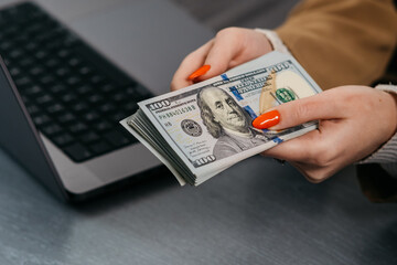 Women's hands hold a stack of money on the background of a laptop computer. The concept of financial savings, banking services, earning money on the Internet. - obrazy, fototapety, plakaty