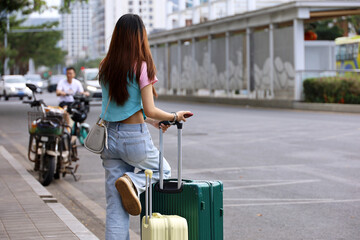 Girl in jeans standing with a suitcases on city street. Concept of travel and summer holidays