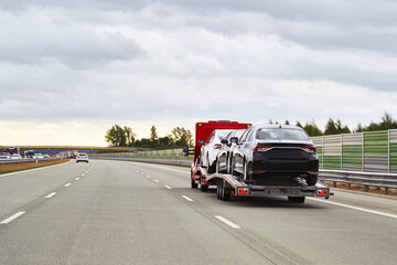 A black SUV is being transported by a yellow tow truck along an empty highway with a cloudy sky overhead.