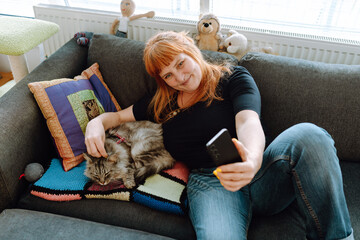 middle-aged woman spends time using phone with pet cat.