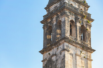 Fototapeta na wymiar Weathered bell tower rises against clear blue sky in Perast, Montenegro; aged stone, arched openings, vegetation sprouting from crevices, baroque architecture. Close up, copy space